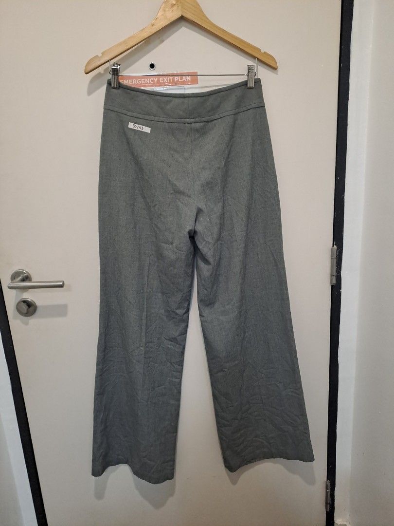 Max Studio gray pants wide leg (Category: Other Bottoms) located in Manila. Submitted by joanbalde39643 (Listing ID 1466440471, Image 3). Description: The image shows a max studio pair of grey wide-leg dress trousers hanging on a wooden hanger against a door. They feature an elegant high-waisted yoke waistband accented with asymmetric side button closures and unique curved, stitched front slash pockets..