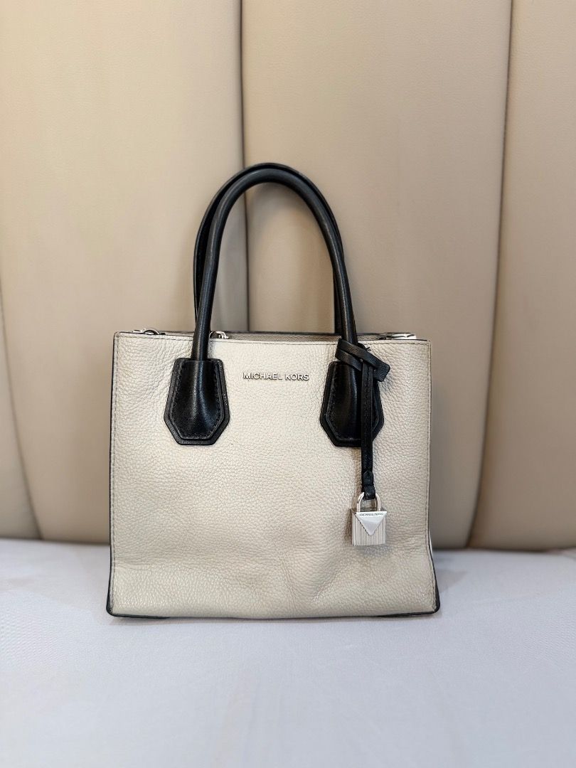 Michael Kors Mercer Tote Bag (Category: Tote Bags) located in Rizal. Submitted by je_resada (Listing ID 1466344793, Image 1). Description: - Brand: Michael Kors - Color: Cream pebble leather with black top handles - Hardware: Silver-toned with dangling padlock charm - Features: Detachable crossbody strap, secure zip compartment inside, and card slots - Condition: Clean interior, bottom feet intact, and minor signs of wear on the handles - Style: 