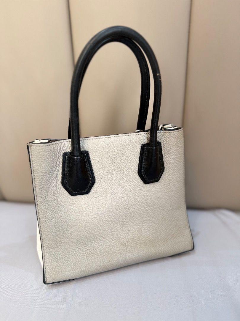 Michael Kors Mercer Tote Bag (Category: Tote Bags) located in Rizal. Submitted by je_resada (Listing ID 1466344793, Image 3). Description: - Brand: Michael Kors - Color: Cream pebble leather with black top handles - Hardware: Silver-toned with dangling padlock charm - Features: Detachable crossbody strap, secure zip compartment inside, and card slots - Condition: Clean interior, bottom feet intact, and minor signs of wear on the handles - Style: 