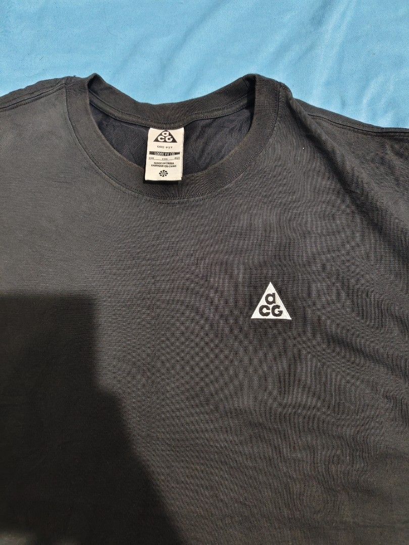 Nike ACG (Category: Tshirts & Polo Shirts ) located in Manila. Submitted by vicious1419 (Listing ID 1466484003, Image 2). Description: Black Nike ACG t-shirt in size XXL. Loose fit style with Dri-FIT material. Small white ACG triangle logo embroidered on the left chest. Large orange and white ACG graphic printed across the back. Tag shows 63% polyester and 37% cotton blend. ISSUE : LAST PHOTO W-23 L-29.