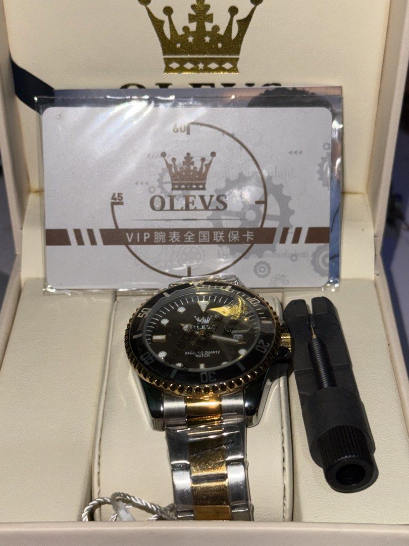 Olevs Dazzling Quartz Watch Gold Silver Two Tone (Category: Women's Watches) located in Paranaque City. Submitted by annann128 (Listing ID 1466560989, Image 3). Description: - Brand: Olevs Quartz Watch - Colorway: Black, Gold, and Silver - Condition: Brand new, unworn, with factory plastics still attached on the bracelet - Features: Rotating bezel and date window at the 3 o'clock position - Strap: Two-tone steel bracelet - Inclusions: Original br