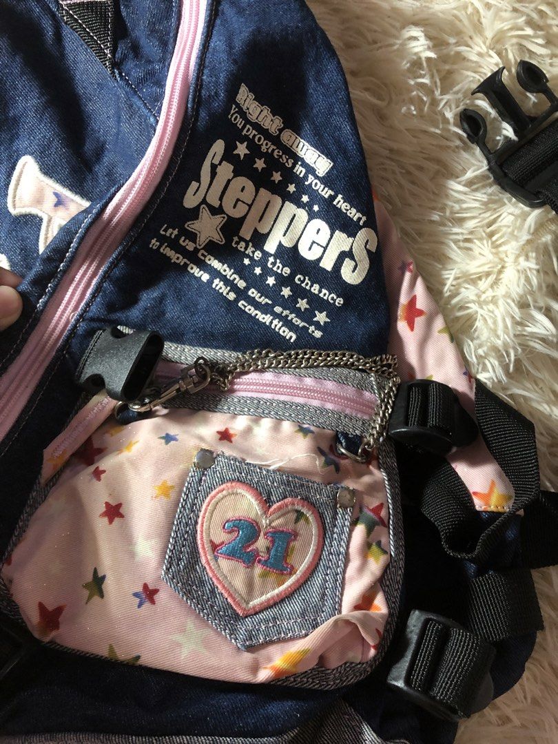 Pink Cross Body Bag Y2k (Category: Cross-body Bags) located in Maria Aurora. Submitted by kylerikathriftshop101010 (Listing ID 1466513704, Image 3). Description: no issues - Style: Vintage street style denim sling backpack with grey and pastel pink accents - Design: Pink star pattern, large embroidered 'pink' text, and 'Steppers' graphics on the front - Storage: Small front pouch with a mini heart pocket, '21' patch, and attached chain detail - C