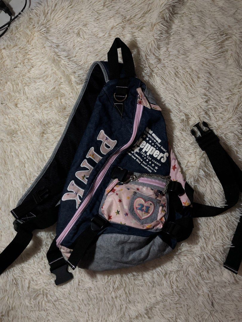 Pink Cross Body Bag Y2k (Category: Cross-body Bags) located in Maria Aurora. Submitted by kylerikathriftshop101010 (Listing ID 1466513704, Image 1). Description: no issues - Style: Vintage street style denim sling backpack with grey and pastel pink accents - Design: Pink star pattern, large embroidered 'pink' text, and 'Steppers' graphics on the front - Storage: Small front pouch with a mini heart pocket, '21' patch, and attached chain detail - C