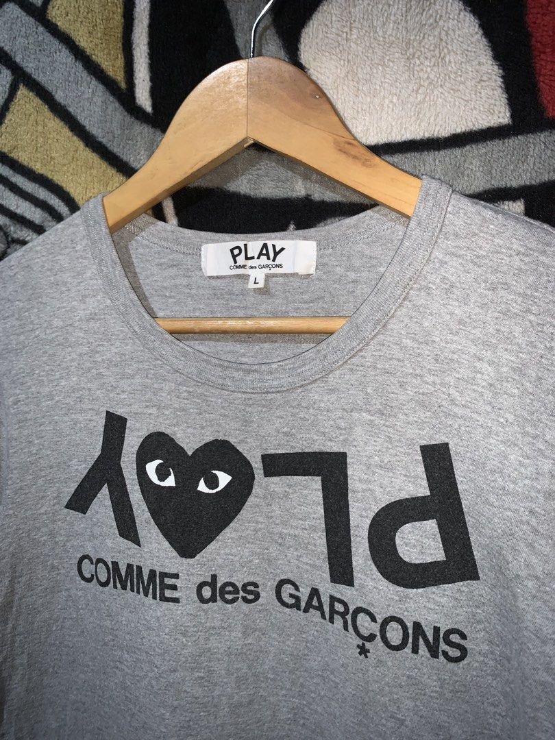 PLAY CDG TEE AUTHENTIC (Category: Shirts) located in Tayug. Submitted by cvcthrift (Listing ID 1466506555, Image 2). Description: 19/26 ISSUE CUT OTHER WASHTAGS EXCELLENT CR-9.5/10 - Authentic Comme des Garçons Play t-shirt - Color: Grey - Size: Large (tag at neck collar) - Design: Bold black Play graphic with heart logo and printed lettering on the front - Details: Includes inner tag with red heart logo and product code (AZ-T...) - Condition: Ex