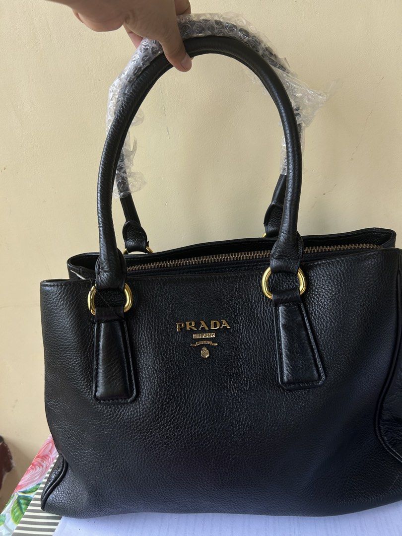 Prada Black Leather Tote Handbag (Category: Luxury Bags & Wallets) located in Valencia. Submitted by carmzfindsph (Listing ID 1466487693, Image 1). Description: - Brand: Prada - Material: Black grained leather - Hardware: Gold-tone with metal logo lettering - Handles: Double top handles (original bubble wrap protective covering still attached) - Closure: Secure zip top closure with expandable side zippers - Interior: Fabric-lined with 1 zip pocke