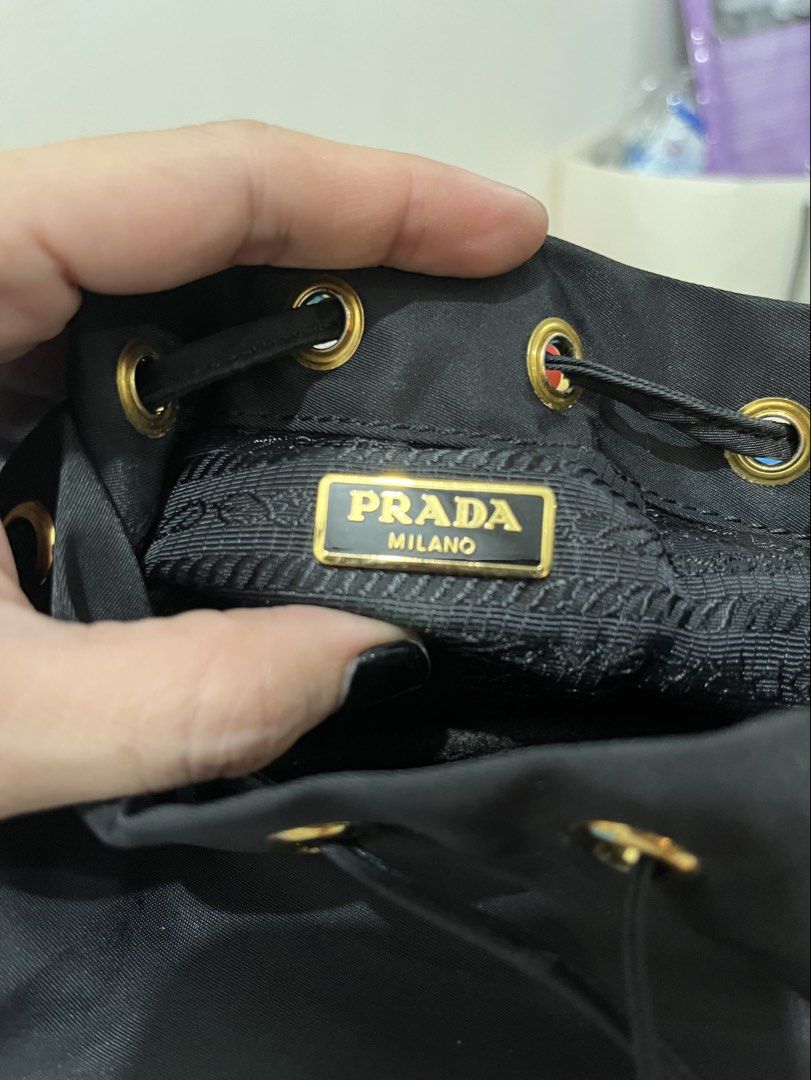 Prada Black Nylon Small Handy Bucket Bag (Category: Purses & Pouches) located in Talisay. Submitted by cherylu (Listing ID 1466551828, Image 2). Description: Black nylon backpack from Prada. Gold hardware throughout, drawstring closure with top handle, front zip pocket with iconic triangle logo plaque. Lampo zipper. Interior fabric lining featuring Prada logo pattern with zippered pocket and Made in Italy tag. Compact everyday size in classic bla