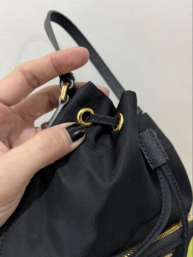 Prada Black Nylon Small Handy Bucket Bag (Category: Purses & Pouches) located in Talisay. Submitted by cherylu (Listing ID 1466551828, Image 3). Description: Black nylon backpack from Prada. Gold hardware throughout, drawstring closure with top handle, front zip pocket with iconic triangle logo plaque. Lampo zipper. Interior fabric lining featuring Prada logo pattern with zippered pocket and Made in Italy tag. Compact everyday size in classic bla