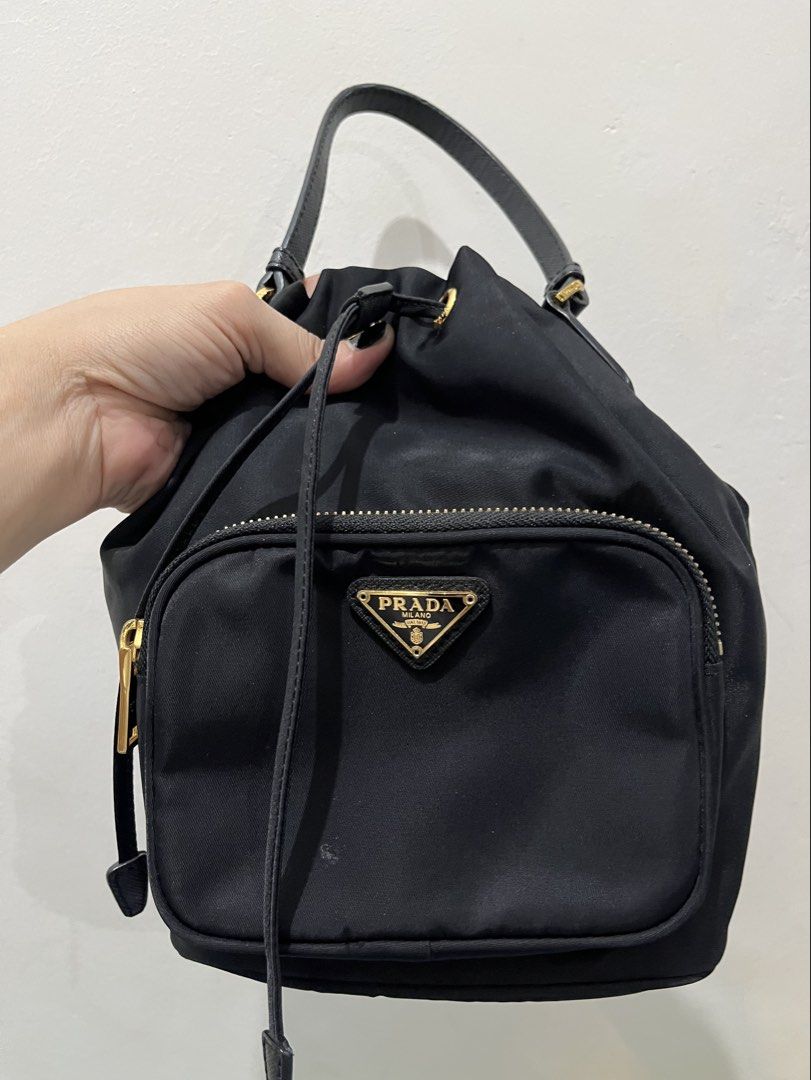 Prada Black Nylon Small Handy Bucket Bag (Category: Purses & Pouches) located in Talisay. Submitted by cherylu (Listing ID 1466551828, Image 1). Description: Black nylon backpack from Prada. Gold hardware throughout, drawstring closure with top handle, front zip pocket with iconic triangle logo plaque. Lampo zipper. Interior fabric lining featuring Prada logo pattern with zippered pocket and Made in Italy tag. Compact everyday size in classic bla