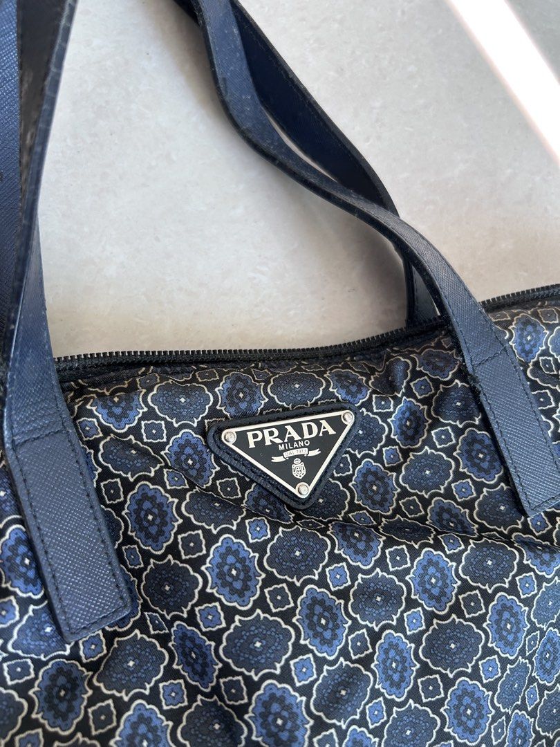 Prada Blue Patterned Nylon Tote Bag with Strap （分類：手袋及銀包）位於 Hong Kong。 由 2019jenjen 提交（商品編號 1466432606，圖片 2）。簡介： Pre-owned Prada Tessuto Stampato Tote Prada tote bag in blue and black patterned fabric. Double top handles plus an extra detachable shoulder strap still wrapped up. (two way wearing) Zip top closure. Signature triangle metal logo on the front. Interior lined with Prada logo fabric, includes a zip pocket and a slip pocket with a metal 