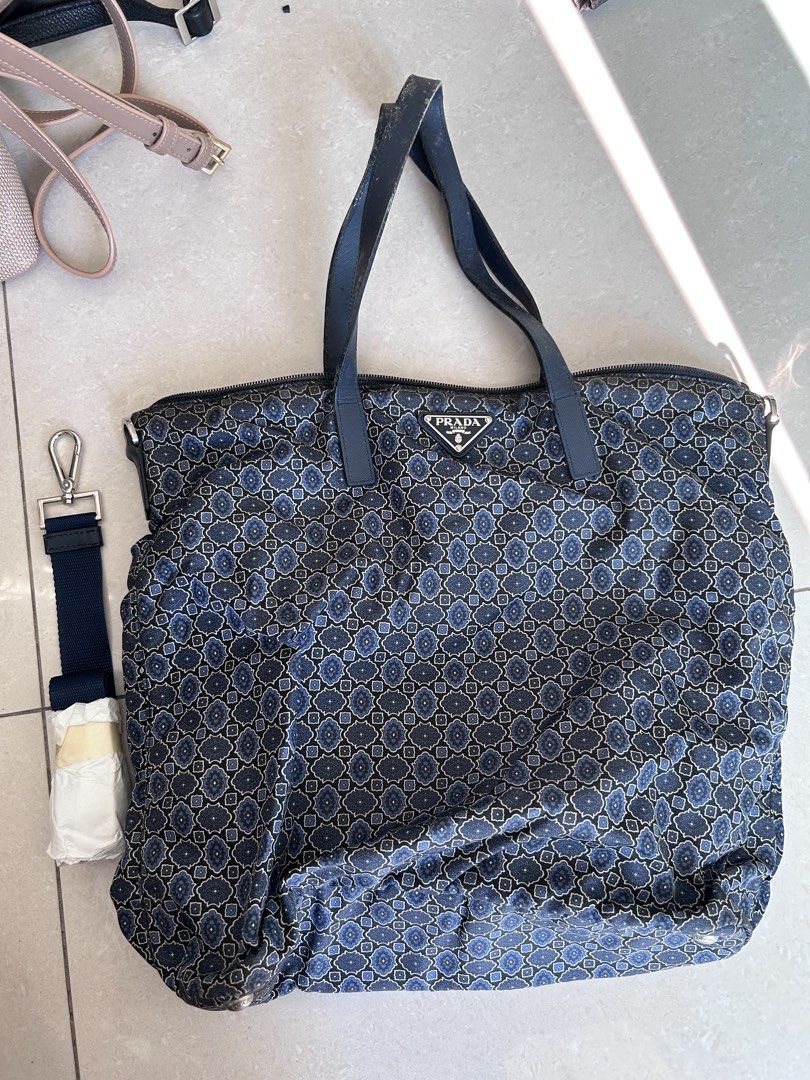 Prada Blue Patterned Nylon Tote Bag with Strap （分類：手袋及銀包）位於 Hong Kong。 由 2019jenjen 提交（商品編號 1466432606，圖片 1）。簡介： Pre-owned Prada Tessuto Stampato Tote Prada tote bag in blue and black patterned fabric. Double top handles plus an extra detachable shoulder strap still wrapped up. (two way wearing) Zip top closure. Signature triangle metal logo on the front. Interior lined with Prada logo fabric, includes a zip pocket and a slip pocket with a metal 