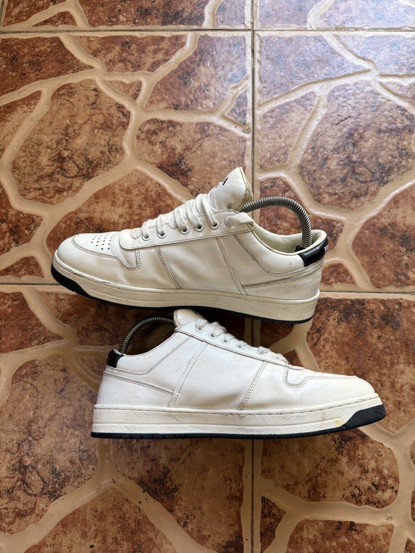 Prada Downtown Leather Low Top Sneakers “Authentic” (Category: Sneakers) located in Cavite. Submitted by stolengoods116 (Listing ID 1466377048, Image 2). Description: - Brand: Prada - Color: White leather with black contrast heel details - Features: Iconic enameled metal triangle logo on the side, Prada branding on tongue and midsole - Design: Classic court shoe silhouette with a perforated toe box for breathability - Condition: Shows minor creas
