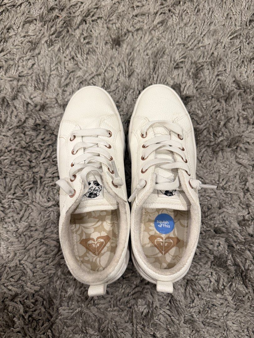 Roxy White Casual Sneakers (Category: Sneakers) located in Pasig City. Submitted by CuratedProj (Listing ID 1466473238, Image 1). Description: - Brand: Roxy - Color: White with rose gold accents - Material: Leather-look finish - Details: Rose gold eyelets, floral printed insoles with Roxy heart logo, and 'squish this' cushioned insoles for extra comfort - Features: Convenient back heel pull tabs and clean white outsoles - Style: Versatile slip-on