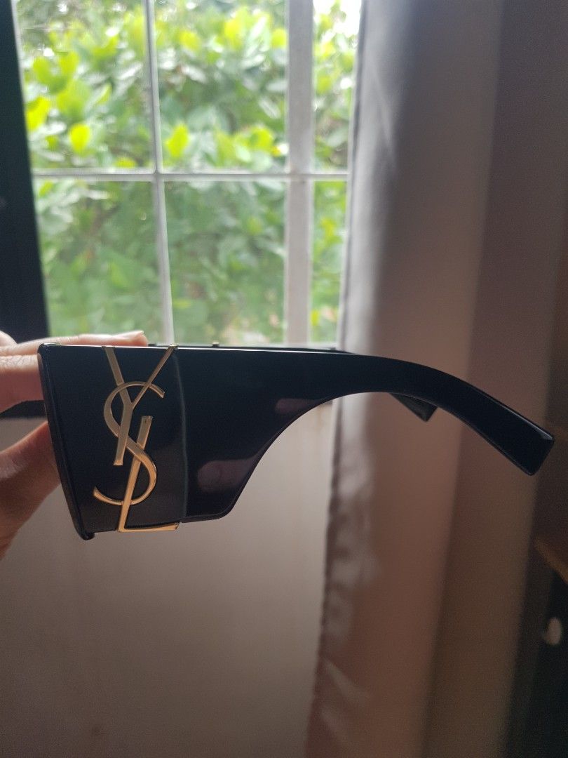 Saint Laurent Sunglasses with YSL Monogram Black (Category: Sunglasses & Eyewear) located in Manila. Submitted by anthonylee23810 (Listing ID 1466449749, Image 2). Description: Black frames with dark tinted lenses. Gold YSL monogram logo on the temples. Thick arm design. Includes a Dolce & Gabbana box and dust pouch. Box shows minor wear. Clean lenses and frames overall. Ready to wear..