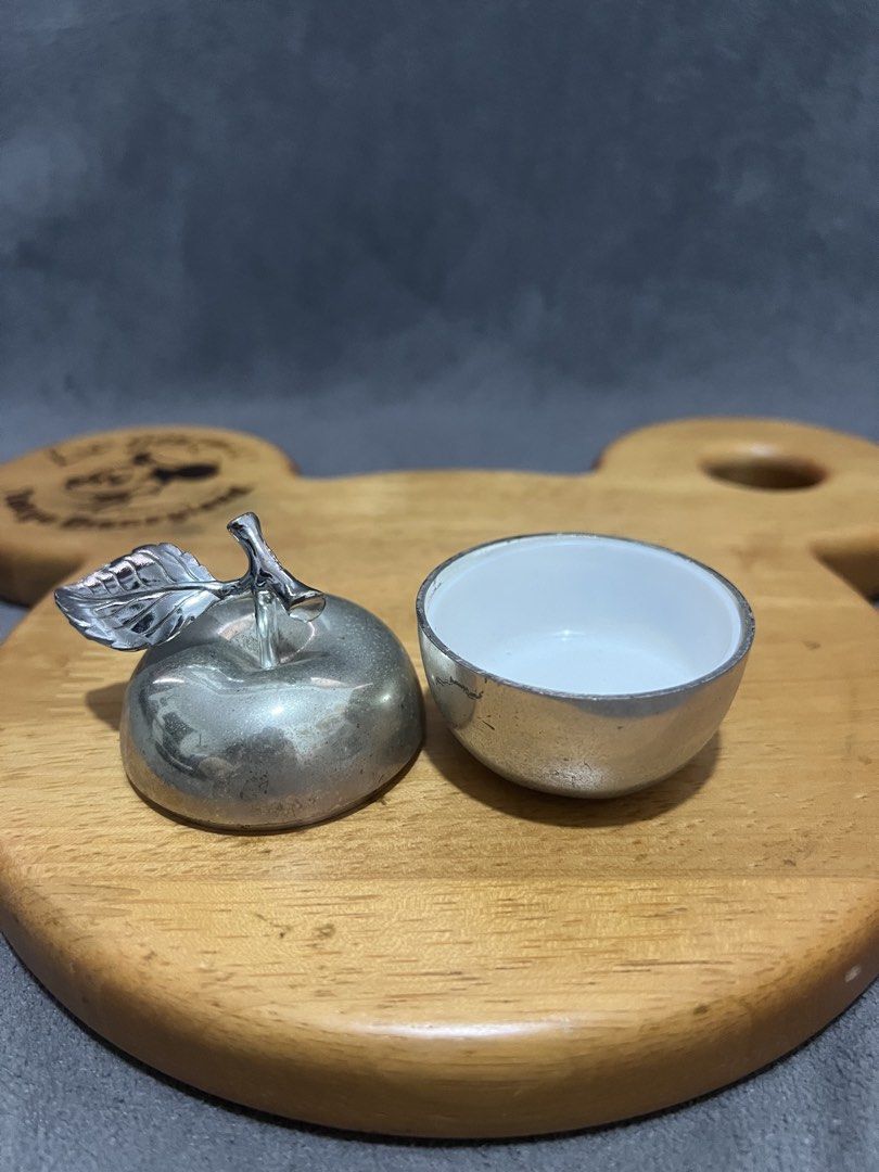 Silver Apple Shaped Trinket Box with Lid (Category: Accessory Holder, Box & Organizers) located in Las Pinas. Submitted by maple0305 (Listing ID 1466413520, Image 3). Description: Silver-toned metal apple trinket box with a stem and leaf handle. Inner bowl is white ceramic or enamel. Cute little container for small jewelry, pills, or desk bits. Lid fits right on top with a small cutout for a spoon or just easy lifting. Polished silver finish with
