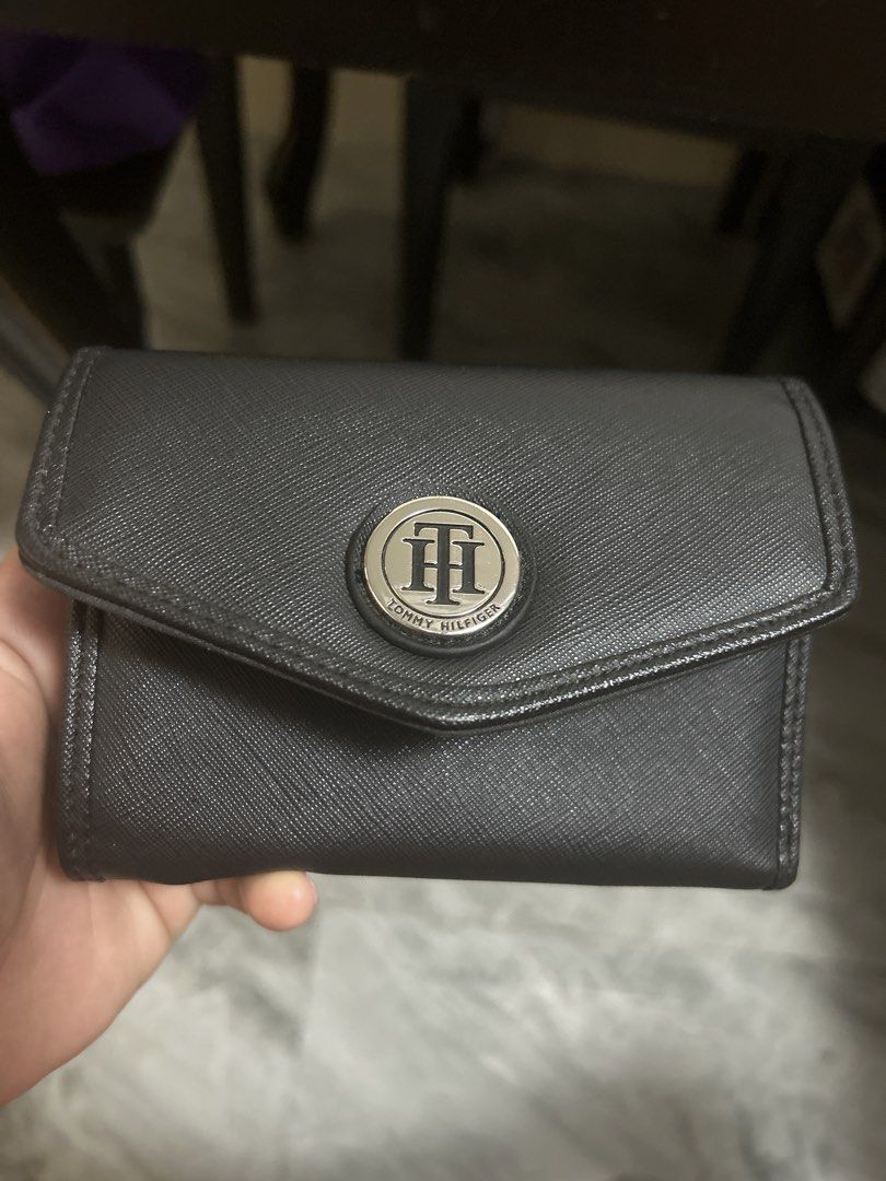 Tommy Hilfiger Black Trifold Wallet (Category: Wallets & Card holders) located in Gapan. Submitted by mysticrabbit-3195 (Listing ID 1466473849, Image 1). Description: - Brand: Tommy Hilfiger - Color: Classic Black - Material: Textured faux leather with silver-tone TH logo badge - Closure: Secure snap button - Interior: Multiple card slots, clear ID window, and spacious cash compartments - Exterior: Back zipped coin pocket with a branded zipper pu