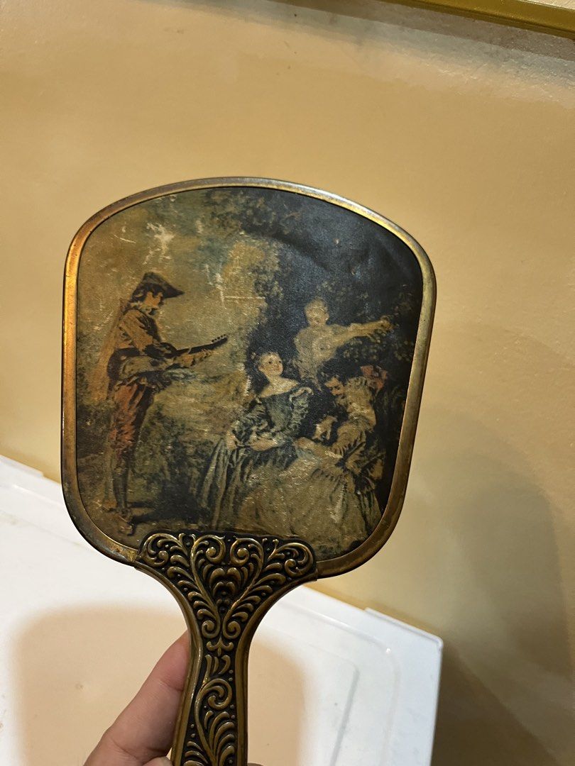 Vintage Handheld Vanity Mirror with Classical Art Print (Category: Mirrors) located in Dasmarinas. Submitted by emmakim08 (Listing ID 1466336783, Image 3). Description: - Vintage hand mirror featuring a classic 18th-century art print on the back - Ornate gold-tone metal frame and handle with intricate scrollwork and floral relief - Clear, high-quality reflective glass on the front - Standard vanity size, ideal for dressers or vanity tables - Cond
