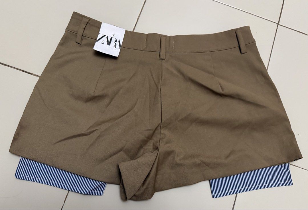 Zara Khaki Skort with Blue Stripe Layer (Category: Shorts) located in Angeles City. Submitted by thon-thal (Listing ID 1466414419, Image 3). Description: Khaki skort from Zara with a layered design. Exposed blue and white striped fabric peeking out at the bottom hem. Front button closure and belt loops. Tailored front panel over built-in shorts. Back tag still attached. size 30 .
