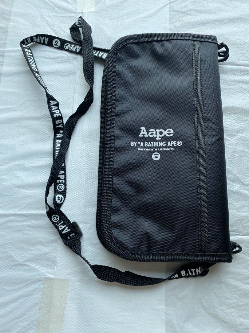 AAPE BY A BATHING APE 黑色頸繩銀包 （分類：手袋及銀包）位於 Hong Kong。 由 hellomami 提交（商品編號 1466591026，圖片 2）。簡介： AAPE 黑色長銀包，有品牌經典猿人頭 Logo 同埋字母印花。附送同款字樣黑色掛頸繩，方便出街掛頸或者斜孭。入面有多個卡位同隔層，放到好多卡同現金，拉鍊開合好安全。尺寸大約 21cm 長，實用又易襯。 型人必選系列，出街、去旅行都啱用。