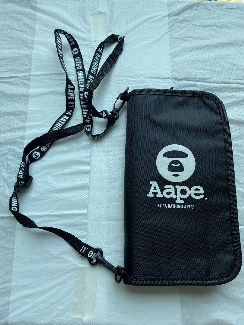 AAPE BY A BATHING APE 黑色頸繩銀包 （分類：手袋及銀包）位於 Hong Kong。 由 hellomami 提交（商品編號 1466591026，圖片 1）。簡介： AAPE 黑色長銀包，有品牌經典猿人頭 Logo 同埋字母印花。附送同款字樣黑色掛頸繩，方便出街掛頸或者斜孭。入面有多個卡位同隔層，放到好多卡同現金，拉鍊開合好安全。尺寸大約 21cm 長，實用又易襯。 型人必選系列，出街、去旅行都啱用。