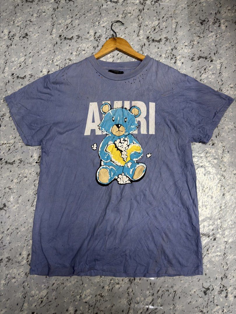 Amri Blue Teddy Bear Graphic Tee Distressed (Category: Activewear) located in Manila. Submitted by raven236 (Listing ID 1466720745, Image 1). Description: - Brand/Style: Amri blue casual streetwear t-shirt - Design: Large front teddy bear graphic with bold white lettering behind it - Details: Short sleeves, classic crew neck collar - Material: Soft and comfortable cotton feel - Special Feature: Pre-distressed fabric style featuring intentional ti