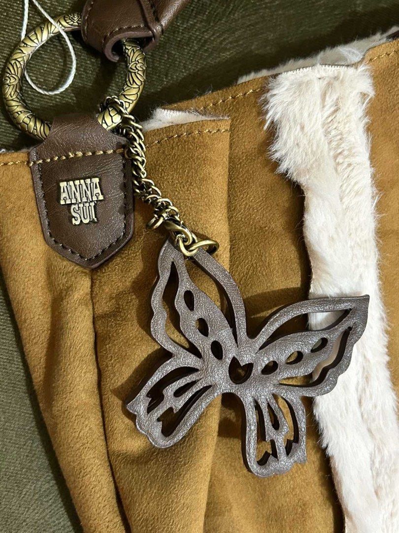 Anna Sui Brown Shoulder Bag with Butterfly Charm (Category: Shoulder Bags) located in Quezon City. Submitted by rosell.xoxo (Listing ID 1466612287, Image 2). Description: - Brand: Anna Sui - Material: Tan suede-style fabric with white fluffy faux fur trim - Straps & Hardware: Brown leather strap with matching brass-toned hardware - Accent: Detachable grey cutout butterfly charm pendant - Details: Gold-lettering Anna Sui brand badge on a brown tab
