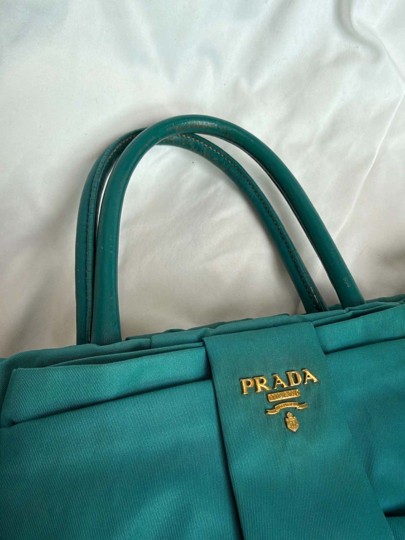 Authentic Prada Tessuto Fiocco Teal Nylon Bow Tote Bag (Category: Luxury Bags & Wallets) located in Marikina City. Submitted by aussiemaan (Listing ID 1466631508, Image 2). Description: Prada Tessuto Fiocco tote in a teal green shade. Nylon body with matching leather handles and trim. Large statement bow on the front with gold-tone Prada logo lettering. Magnetic snap closure on top, zip pocket inside. Signature patterned lining. Bottom feet for p