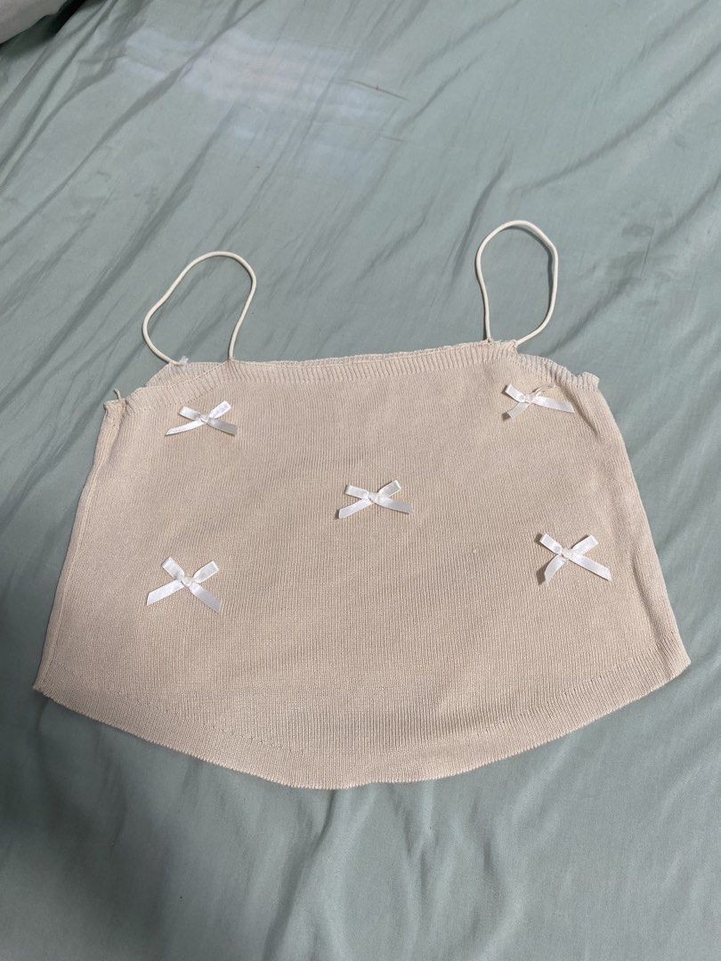 Beige Knit Camisole with White Bows (Category: Sleeveless) located in Las Pinas. Submitted by andwe_yaa (Listing ID 1466612189, Image 1). Description: - Color: Beige - Material: Soft ribbed knit - Design: Thin spaghetti straps and a flattering curved hem - Detail: Five charming white satin bows scattered on the front - Style: Dainty, cute, and casual - Pairing: Perfect to match with high-waisted jeans or skirts -May need extra stitching of Straps