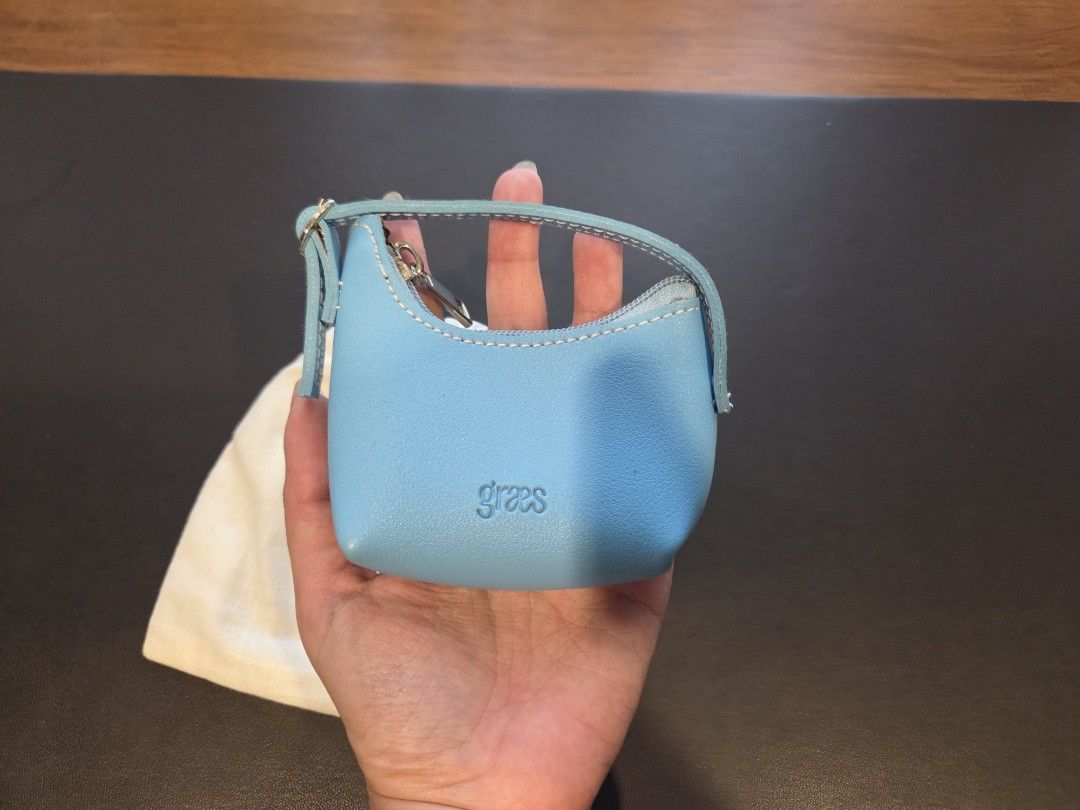 [Brand New] Graes Light Blue Coin Wallet (Category: Wallets & Card Holders) located in Manila. Submitted by liza1003 (Listing ID 1466625663, Image 2). Description: - Brand: Graes - Style: Mini wallet with top handle - Color: Light blue with white contrast stitching - Closure: Top zipper - Size: Mini / palm-sized - Inclusion: White cotton dust bag - Detail: Embossed brand logo on the front 24 hours reservation only No refunds, returns, or exchange