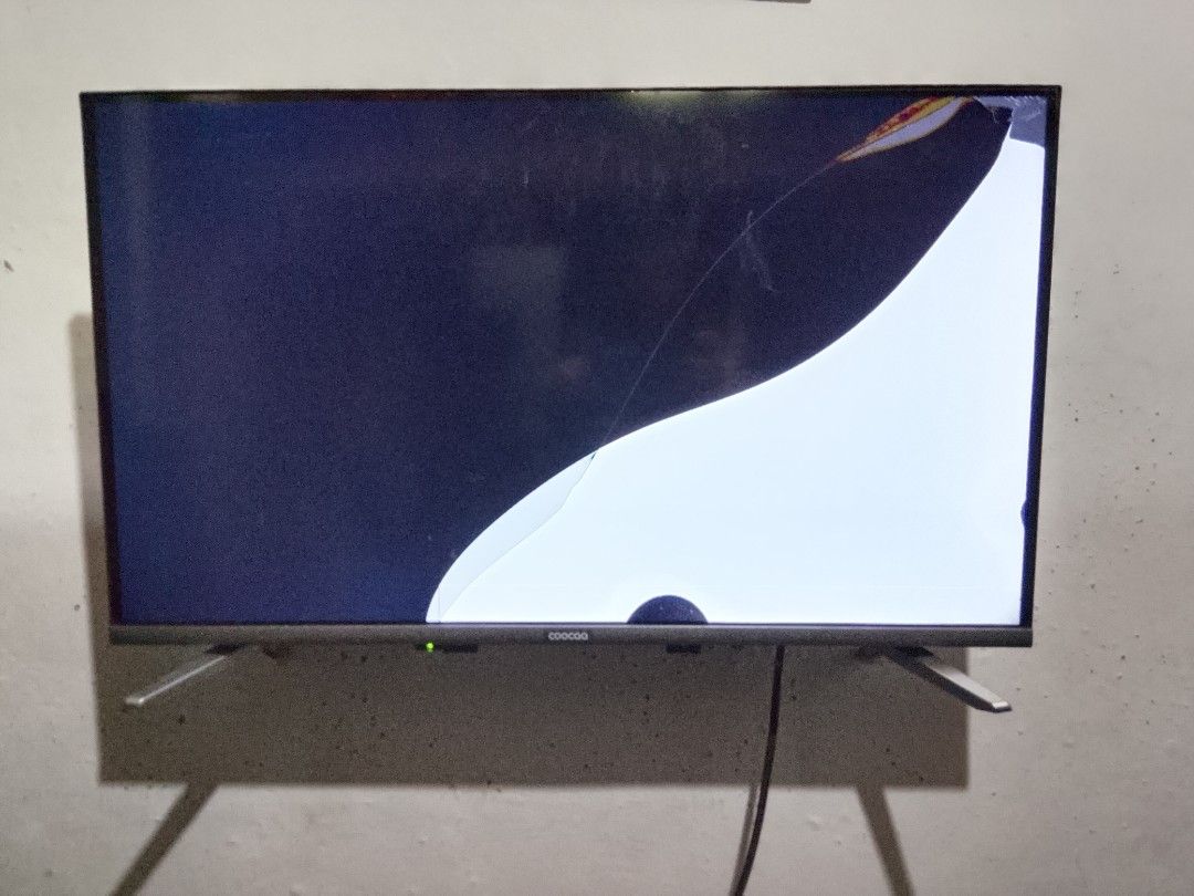 Broken Coocaa television screen (Category: TV) located in Manila. Submitted by roxxdeloss46067 (Listing ID 1466587992, Image 3). Description: - Brand: Coocaa TV - Condition: Screen cracked top right, heavy display distortion - Best for: Spare parts or repair project - Inclusions: Attached stand legs and connected power cable - Delivery: Pick up preferred due to fragile screen state.