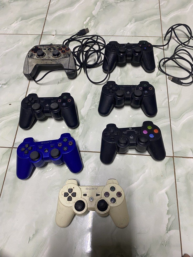 Bundle of Sony PlayStation 2 and 3 Controllers (Category: Controllers) located in Pasacao. Submitted by wengpullar37205 (Listing ID 1466750213, Image 1). Description: - Bundle of 7 PlayStation game controllers (wired and wireless) - Colors include black, blue, white, and custom weathered designs - Includes attached cables and USB connectors - Condition: Heavy dirt, discoloration, scuffs, and wear on housings and thumbsticks - Sold as-is for spare