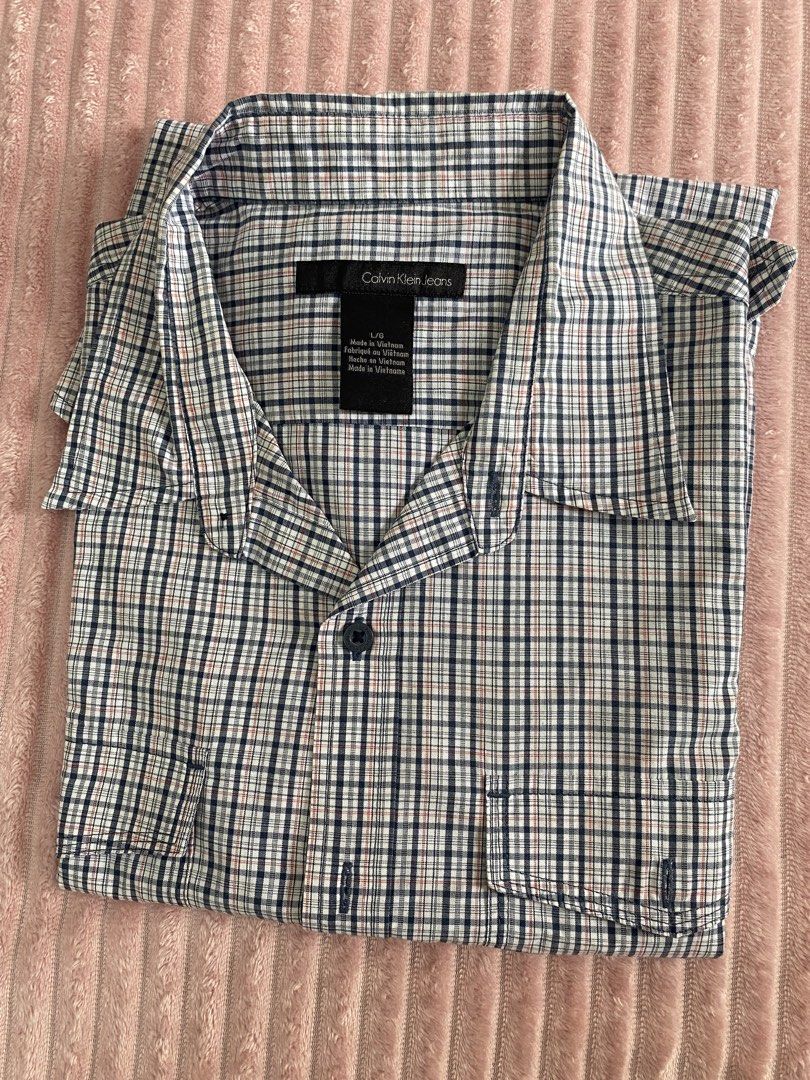 Calvin Klein Jeans Plaid Button-Down Shirt Size L (Category: Tshirts & Polo Shirts ) located in Paranaque City. Submitted by axie1206 (Listing ID 1466599705, Image 1). Description: - Brand: Calvin Klein Jeans - Size: L - Color/Pattern: Navy blue, white, and red plaid check - Features: Standard pointed collar, two front chest pockets with button closures - Origin: Made in Vietnam - Condition: Clean fabric throughout, neat folding lines from storag