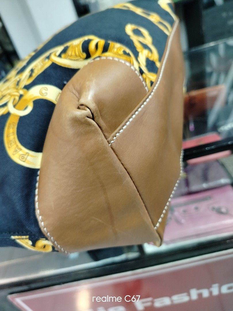 Celine Chain Print Canvas Tote Bag (Category: Luxury Bags & Wallets) located in Bacolod City. Submitted by Mike23MattPreloved (Listing ID 1466627420, Image 3). Description: - Brand: Celine - Material: Navy blue canvas with tan leather trim - Design: All-over gold chain print with sign of use with gold-tone hardware and engraved motifs - Features: Spacious interior, sturdy top handles - Condition: Good, with minor leather wear near handle attachme
