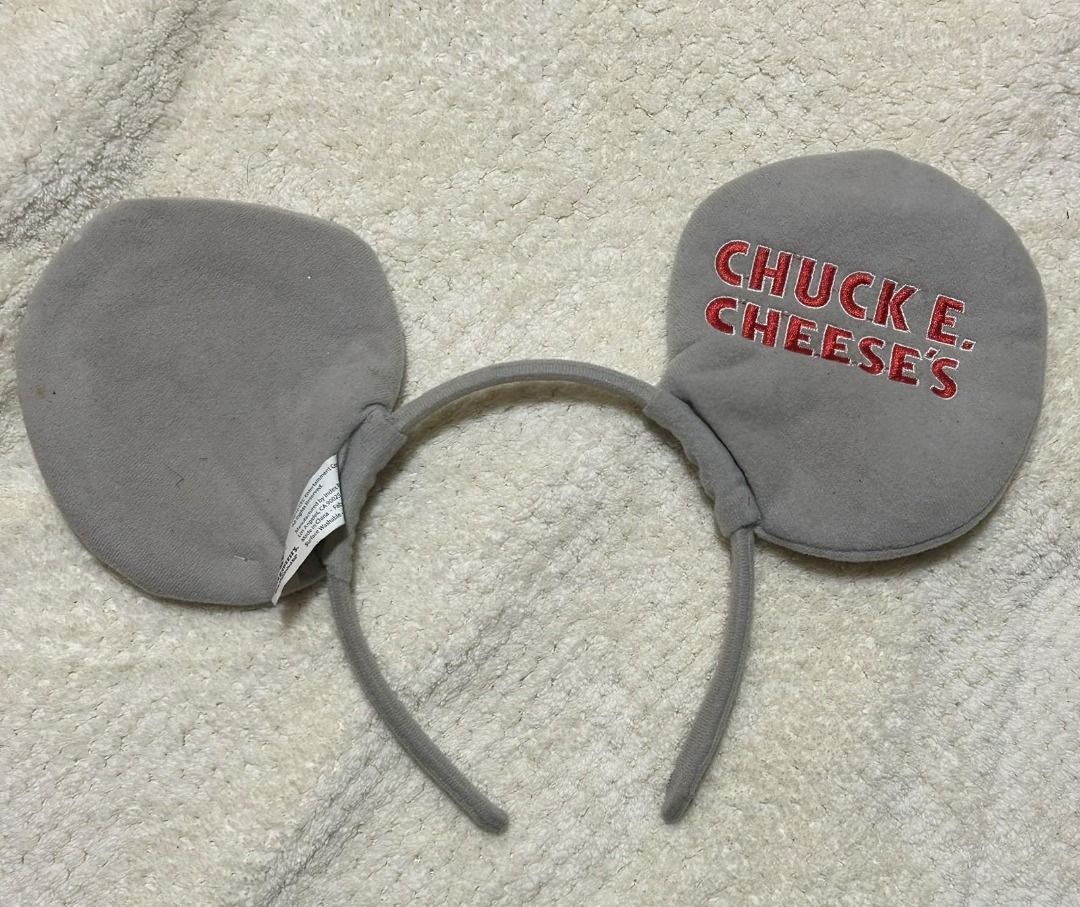 Chuck E. Cheese Mouse Ears Headband (Category: Hair Accessories) located in Las Pinas. Submitted by whatzupriley (Listing ID 1466650494, Image 1). Description: - Official 2016 CEC Entertainment merchandise - Grey mouse ears headband featuring red embroidered text - Comfortable fabric-wrapped headband construction - Includes original manufacturer tag - Condition note: Small orange stain visible on one ear surface.