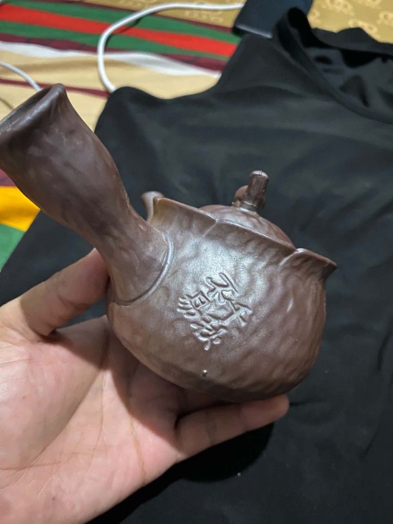Vintage Clay Teapot With Side Handle And Carved Design (Category: Coffee & Tea Tableware) located in Marikina City. Submitted by jvdshop (Listing ID 1466672885, Image 2). Description: - Authentic brown clay teapot with a traditional side handle - Textured body featuring carved Chinese characters and an intricate wheel motif - Includes a matching lid topped with an adorable, sculpted bird - Perfect for brewing loose leaf tea or adding to a traditi