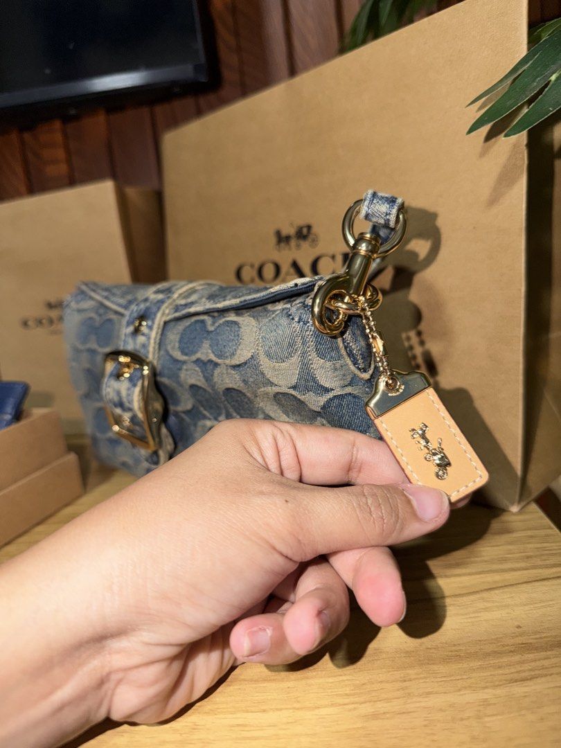 Coach Denim Signature Shoulder Bag (Category: Luxury Bags & Wallets) located in Taguig. Submitted by JHOs.it.up (Listing ID 1466589056, Image 3). Description: - Authentic Coach shoulder bag - Classic blue signature denim monogram print with leather charm - Elegant gold-tone hardware and chic front buckle detail - Structured rectangular shape for everyday use - Complete with tag, and paperbag - Condition: Brand new.