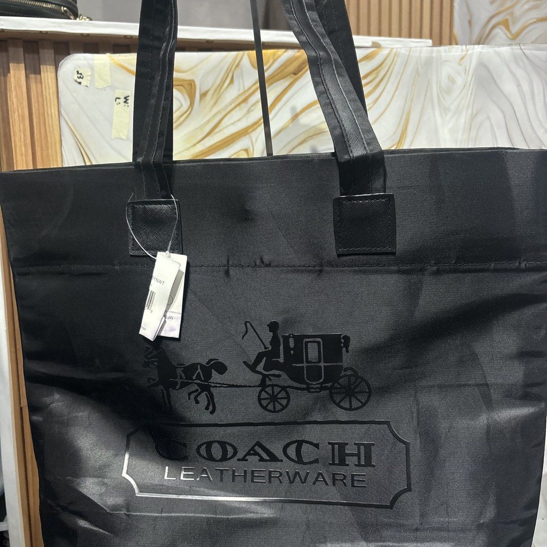 Coach Leatherware Black Nylon Tote Bag (Category: Tote Bags) located in Bambang. Submitted by heats777 (Listing ID 1466663052, Image 3). Description: - Brand: Coach Leatherware - Material: Durable black nylon with black fabric shoulder straps - Design: Large horse and carriage logo printed on the front - Closure: Secure magnetic snap top closure - Interior: Roomy compartment with a zipped pocket and embossed Coach logo - Condition: Brand new with
