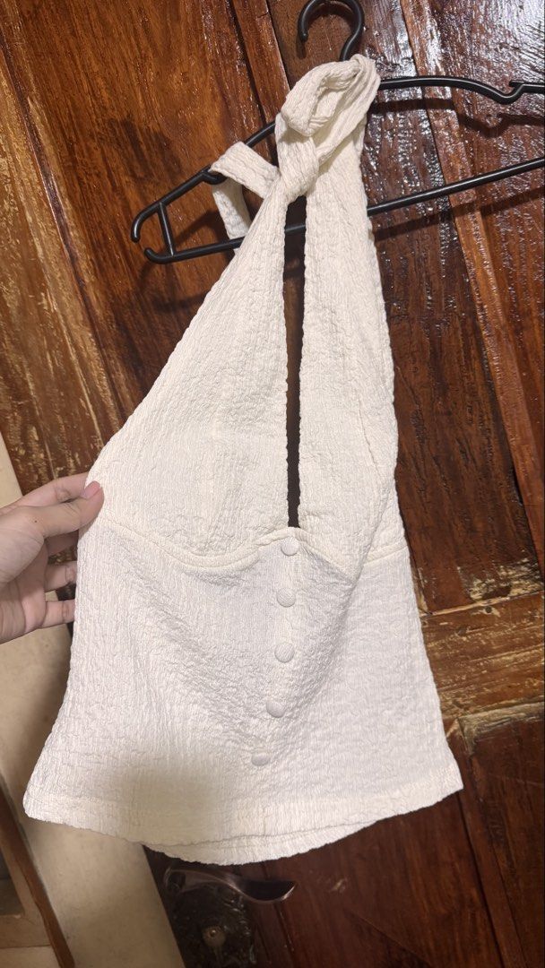 Cream Halter Neck Button Front Textured Crop Top (Category: Sleeveless) located in Kananga. Submitted by yongggi (Listing ID 1466700755, Image 1). Description: Cream textured halter neck top with matching fabric buttons down the front. Deep V-neckline, unstructured back strap tie closure. Stretchy crinkle fabric material. Clean and well-kept piece..