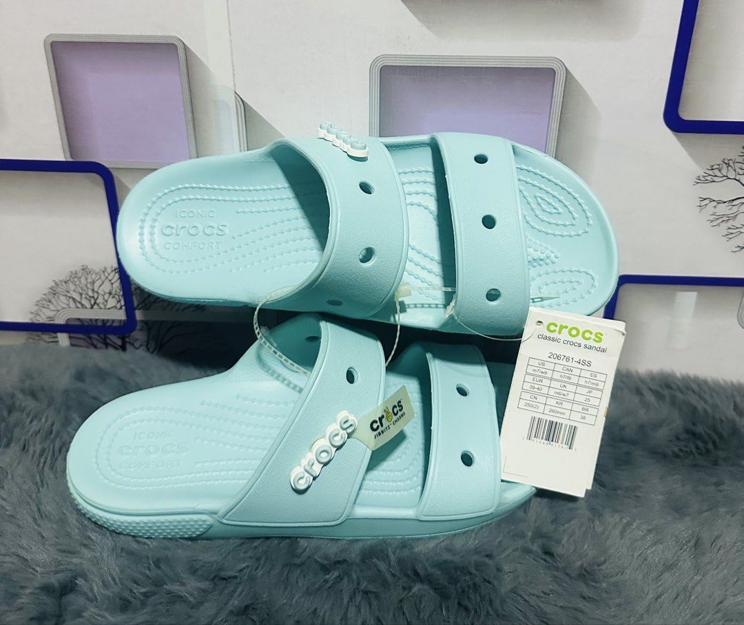 Crocs Classic 2-Strap Sandals Light Blue Size M7/W9 (Category: Flats & Sandals) located in Liloan. Submitted by cnerosel2026 (Listing ID 1466712304, Image 3). Description: - Style: Classic 2-strap slip-on sandals - Color: Light blue with a white Jibbitz charm on the side - Condition: Brand new with original tags attached - Size: US M7 / W9 (EUR 39-40) - Features: Breathable ventilation holes and signature Iconic Crocs comfort footbed - Perfect fo