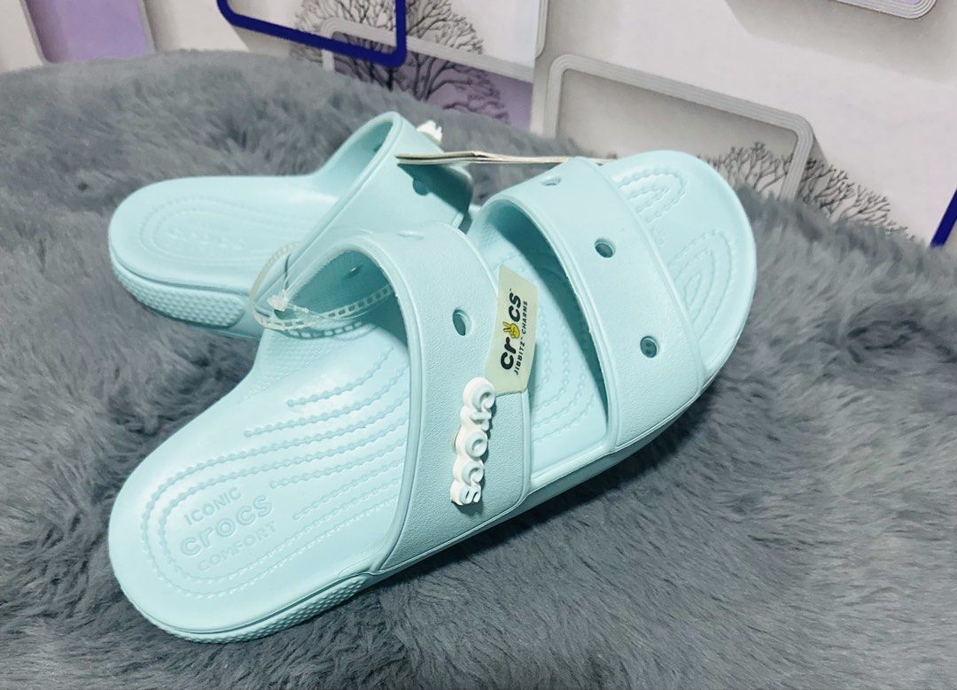 Crocs Classic 2-Strap Sandals Light Blue Size M7/W9 (Category: Flats & Sandals) located in Liloan. Submitted by cnerosel2026 (Listing ID 1466712304, Image 2). Description: - Style: Classic 2-strap slip-on sandals - Color: Light blue with a white Jibbitz charm on the side - Condition: Brand new with original tags attached - Size: US M7 / W9 (EUR 39-40) - Features: Breathable ventilation holes and signature Iconic Crocs comfort footbed - Perfect fo