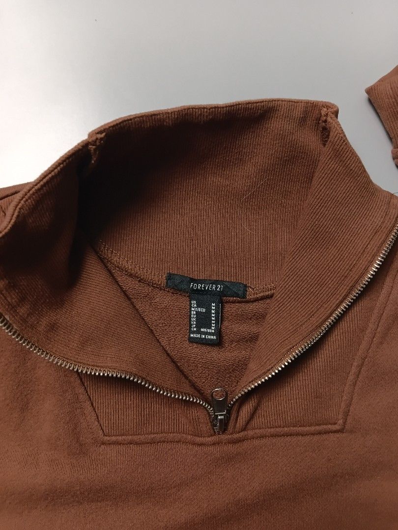 cropped quarter-zip pullover pullover sweatshirt in a medium chocolate brown color. (Category: Coats, Jackets and Outerwear) located in Manila. Submitted by hustler_777 (Listing ID 1466666666, Image 3). Description: Brand: Forever 21 • Sizing: The item is marked as a size Medium (M) across multiple regional sizing formats (US, CA, MX/ECU, BR, EU, UK, KR, JP). • Production Context: The label indicates the garment was Made in China and includes the