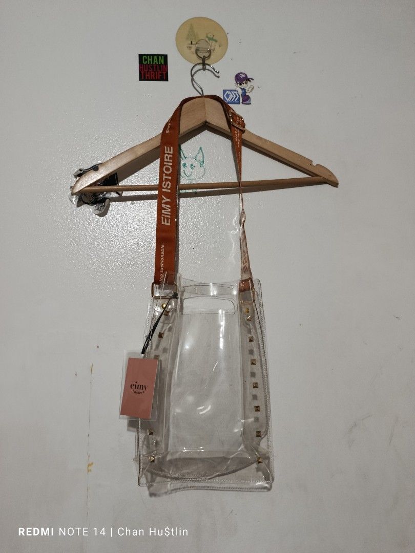 Eimy Istoire Clear Studded Shoulder Bag (Category: Shoulder Bags) located in Calamba. Submitted by chanmagpantay (Listing ID 1466590565, Image 1). Description: - Brand: Eimy Istoire (Authentic with original Japanese store tags) - Material: Durable clear PVC with a structured base - Accents: Chic gold pyramid studs along the sides - Strap: Bold orange fabric strap featuring vertical brand printing - Design: Open top for easy access - Condition: Br