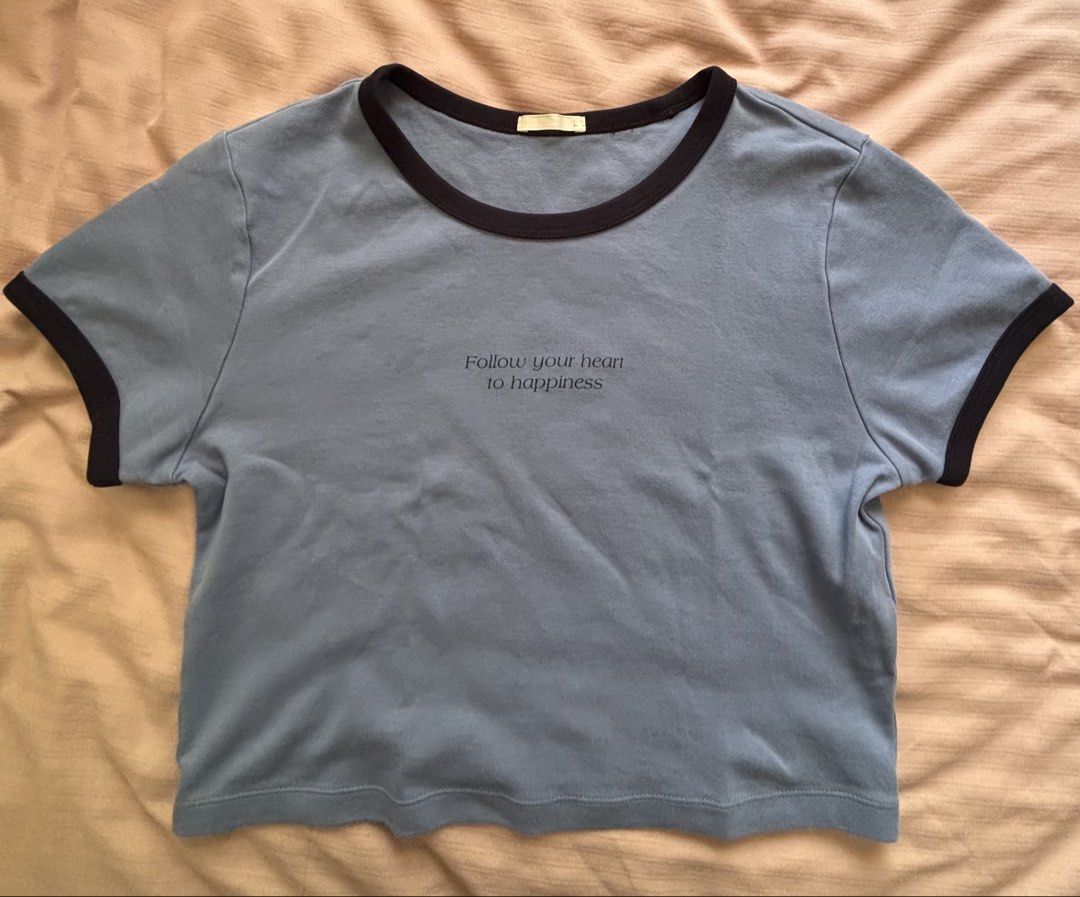 GU Blue Ringer Crop Top Slogan Tee Size L (Category: Shirts) located in Mandaue City. Submitted by jbstl (Listing ID 1466585247, Image 2). Description: - Brand/Style: GU blue crop top with black ringer collar and cuffs - Design: "Follow your heart to happiness" quote print on the chest - Size: L (fits 160/88A) - Material: Comfortable cotton and polyester blend - Fit: Casual style, easy to pair with high-waisted jeans or skirts.
