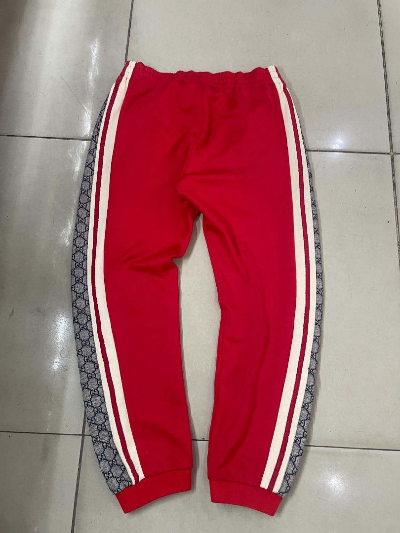 Gucci GG Supreme Side Stripe Red Jogging Pants (Category: Joggers) located in Cainta. Submitted by riszizlux (Listing ID 1466671653, Image 2). Description: - Brand: Gucci - Color: Red with cream taping and GG Supreme canvas side stripes - Size: Medium (M) tag attached - Material: Premium cotton blend, Made in Italy - Features: Elastic waistband with adjustable drawstring, secure zippered front pockets, and ribbed ankle cuffs - Condition: Excellen