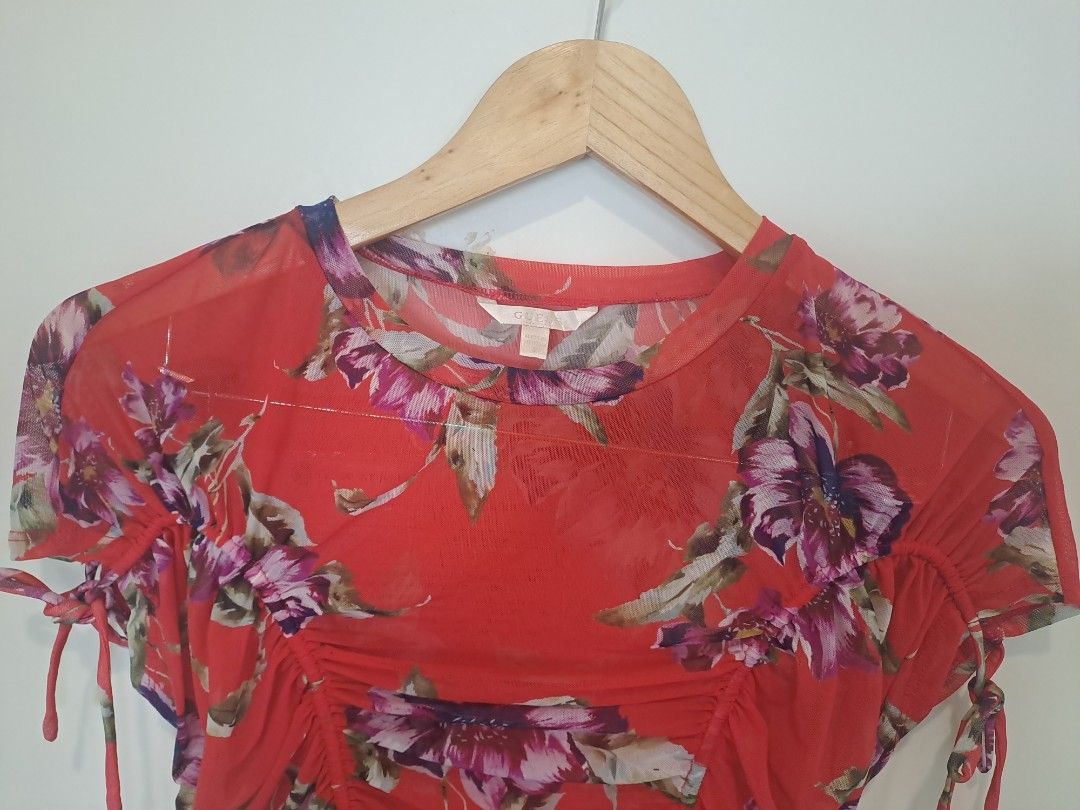 Guess floral mesh (Category: Blouses) located in Manila. Submitted by joanbalde39643 (Listing ID 1466663391, Image 2). Description: This piece is a GUESS vibrant red floral mesh ruched top featuring short cap sleeves with functional drawstring tie details. It showcases an all-over tropical botanical pattern highlighted by purple and magenta hibiscus flowers and is constructed from a lightweight, semi-sheer mesh fabric with central ruched body sha