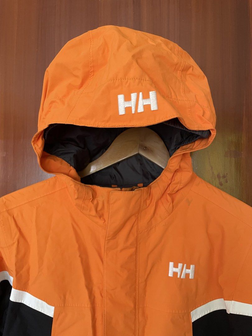 Helly Hansen Orange Black Waterproof Hooded Jacket Size M (Category: Coats, Jackets and Outerwear) located in Cebu City. Submitted by annyeongthriftcebu (Listing ID 1466633923, Image 2). Description: - Brand: Helly Hansen - Color: Bright orange with black and white color blocking - Branding: Bold white HH printed on hood, chest, and back - Features: Zippered front closure with storm flap, high collar, front hand pockets, and gray inner lining - C