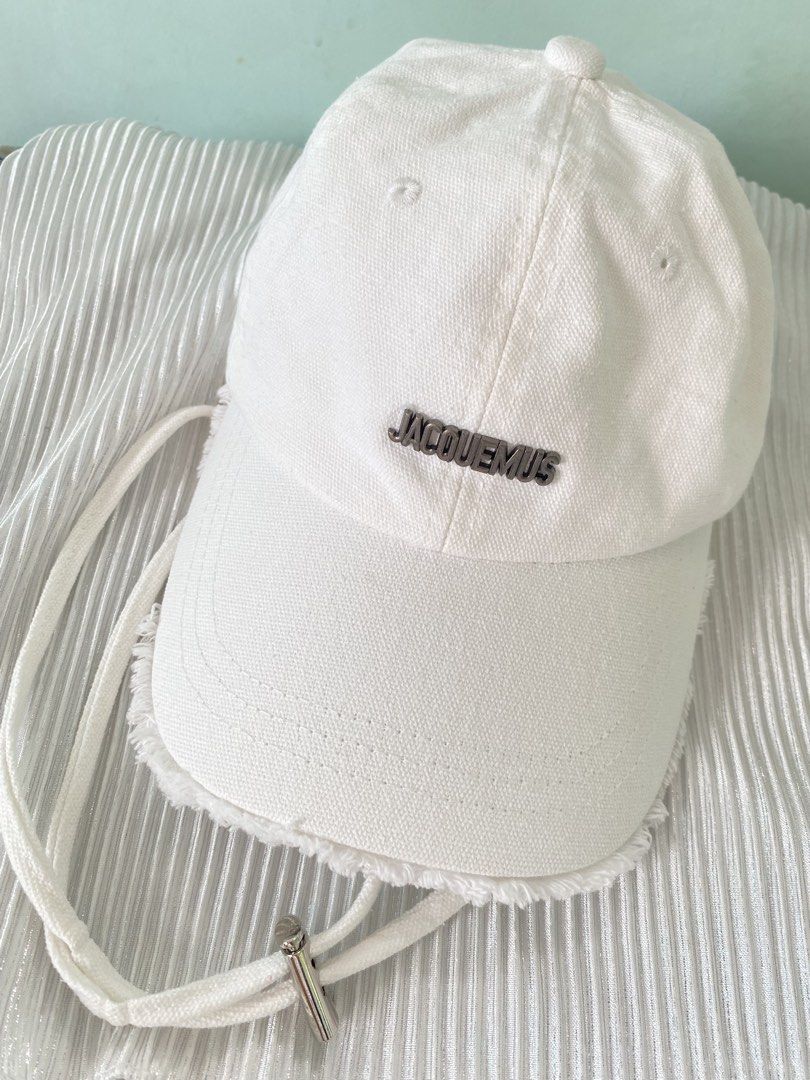 Jacquemus White Baseball Cap with Frayed Edge (Category: Caps & Hats) located in Tabaco. Submitted by camila_p (Listing ID 1466613863, Image 1). Description: - Brand: Jacquemus - Color: Clean White - Material: Canvas - Features: Metal front logo lettering, trendy frayed brim edge - Hardware: Adjustable metal buckle strap with silver-tipped hanging drawstrings - Origin: Made in Bulgaria - Condition: Excellent.