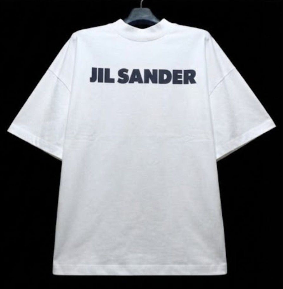 Jil Sander Logo White T-Shirt (Category: Shirts) located in Donsol. Submitted by saksthriftavenuebyluckymaria8 (Listing ID 1466383848, Image 3). Description: - Authentic Jil Sander minimalist white t-shirt - Bold black logo printed across the chest - Classic crewneck with a relaxed, oversized fit - Premium heavy cotton material for a clean, structured look - Highly versatile and easy to style with casual pants or shorts JIL SANDER LOGO shirt Sz L