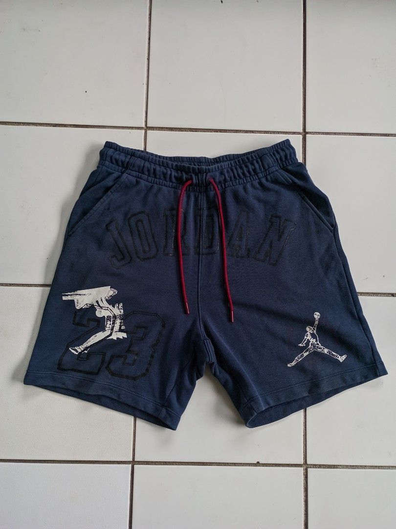 Jordan Essentials Men's Loopback Fleece / Knit Shorts (Category: Shorts) located in Iriga City. Submitted by cxvgarments (Listing ID 1466637242, Image 2). Description: • Color: Navy blue with red drawstrings and white/black graphics. • Details: Features the debossed "JORDAN" arch lettering across the front waistband area, a large "23" graphic with the classic Michael Jordan silhouette on the left leg, and the Jumpman logo on the right leg. • Mate