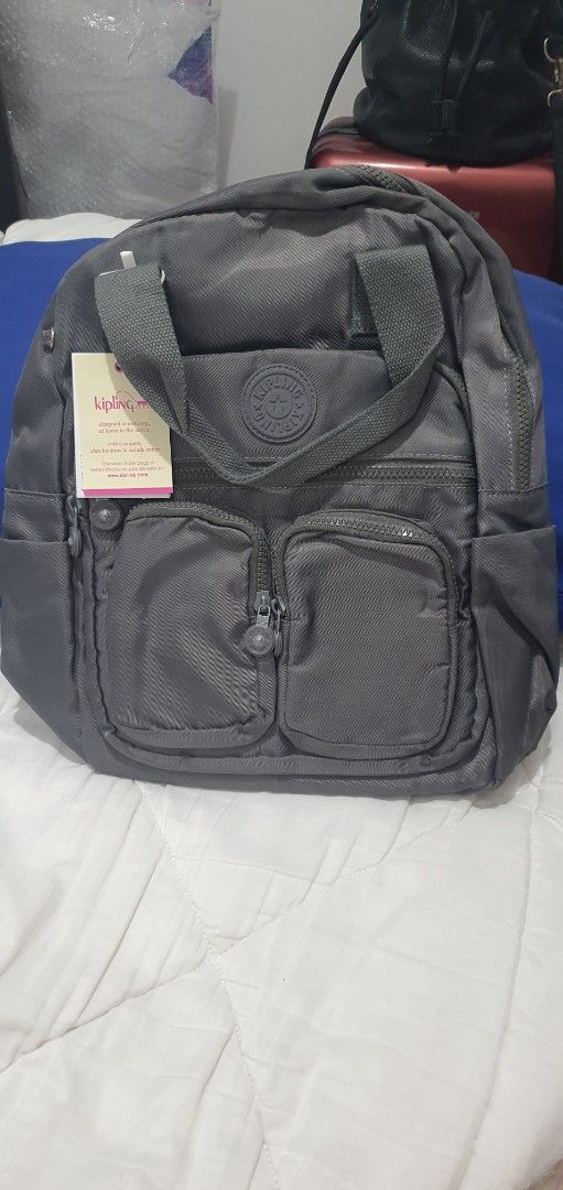 Kipling Grey Backpack with Front Pockets (Category: Backpacks) located in Paranaque City. Submitted by personal_preloved40 (Listing ID 1466656411, Image 2). Description: - Brand: Kipling - Color: Dark grey with grey and white striped interior lining - Condition: Brand new with original tags, kept in protective plastic - Features: Dual zippered front pockets, top grab handle, and adjustable back straps - Interior: Includes convenient slip compartm