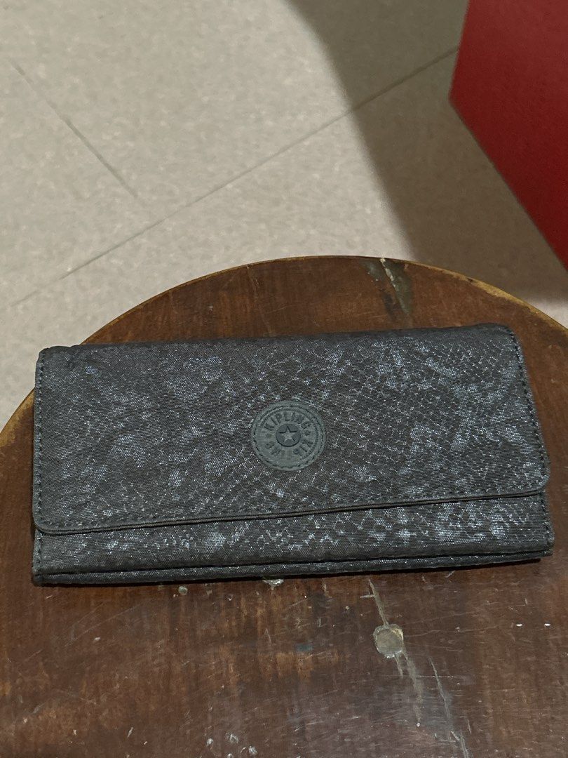 Kipling Long Wallet Dark Grey Textured (Category: Wallets & Card holders) located in Alitagtag. Submitted by patrickvillanueva (Listing ID 1466628867, Image 1). Description: Kipling long wallet in a dark grey textured fabric. Snap button closure on the front flap. Inside has multiple card slots, clear ID windows, bill compartments, and a zippered coin pocket. Shows some yellowing inside the clear ID slots from age and storage. Clean fabric exteri